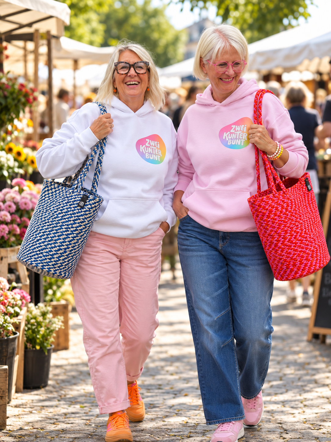 Zwei Frauen mit ZweiKunterbunt-Hoodies und Seiltaschen auf einem Markt (KI-Bild)